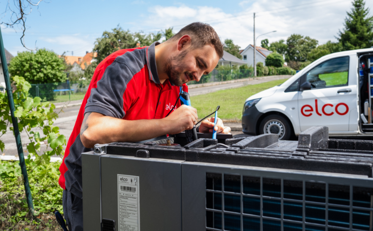 Servicetechnicus werkt aan een verwarmings- of airconditioningsysteem buiten, op de achtergrond een bedrijfswagen van ELCO..